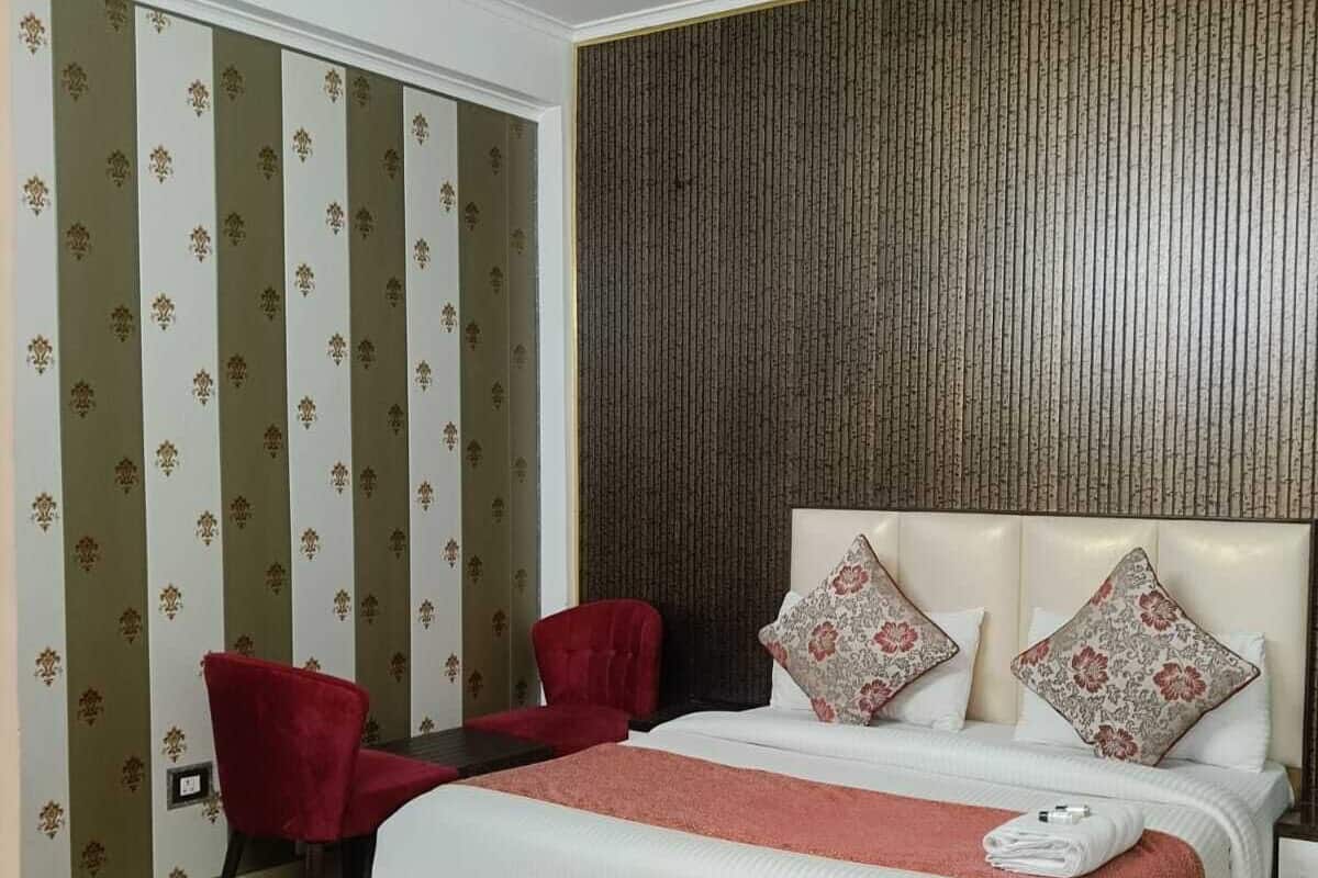 A bedroom with a large bed, two red chairs, a ceiling fan, and patterned wallpaper.