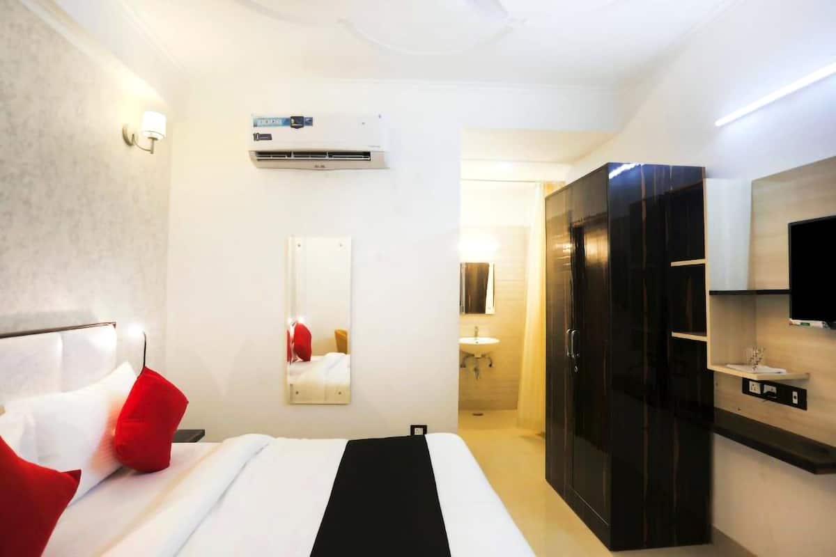 A hotel room with a bed, a wardrobe, a mirror, an air conditioning unit, and a television.