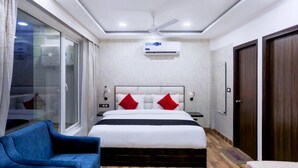 Una habitación de hotel moderna con una cama grande, un sillón azul, piso de madera y un ventilador de techo.