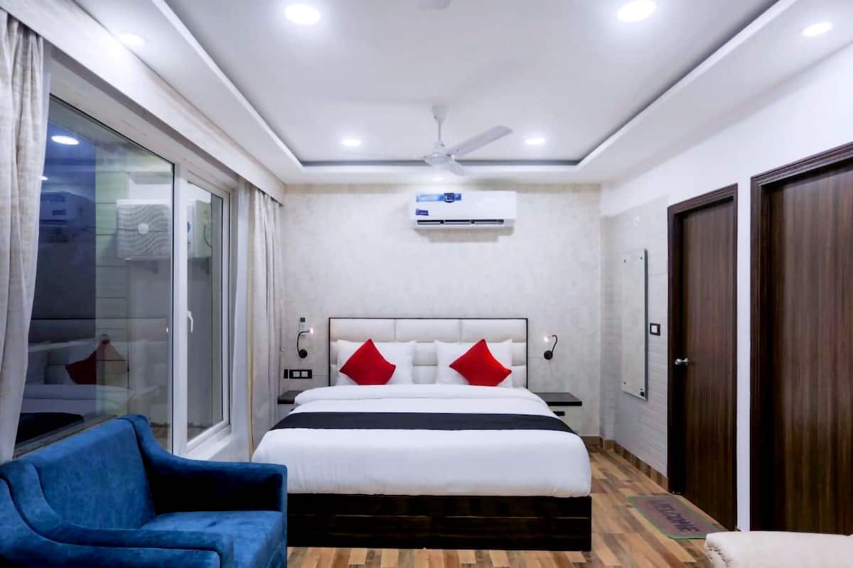 A modern hotel room with a large bed, a blue armchair, a wooden floor, and a ceiling fan.