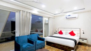 Una habitación de hotel con una cama, un sillón azul, una mesa redonda y un ventanal con cortinas.