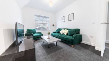Un salon moderne avec un meuble en bois foncé, un canapé vert, une table basse blanche et une fenêtre avec des stores.