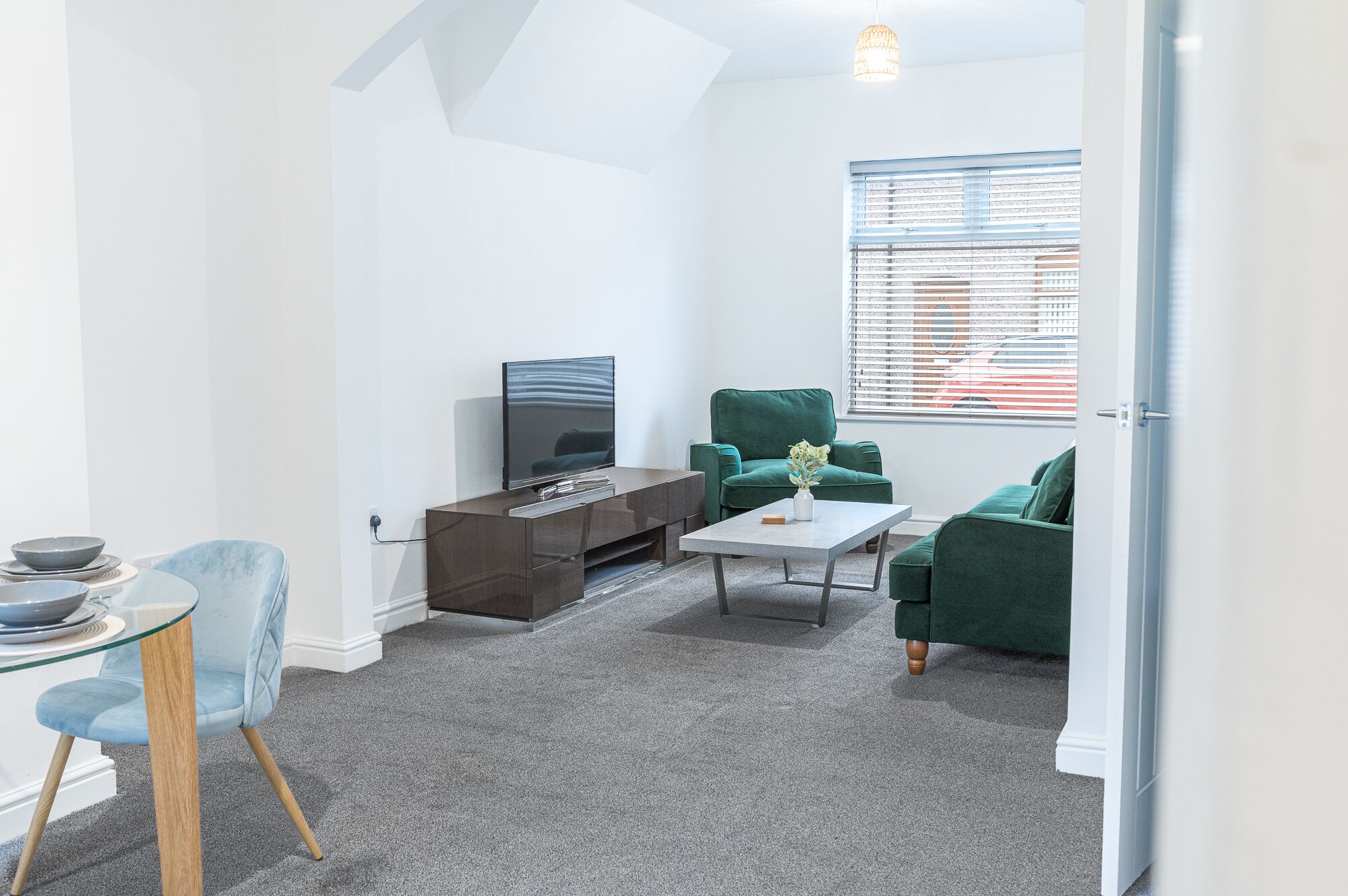 A modern living room with a flat-screen TV, a green sofa, a glass coffee table, and a blue chair.