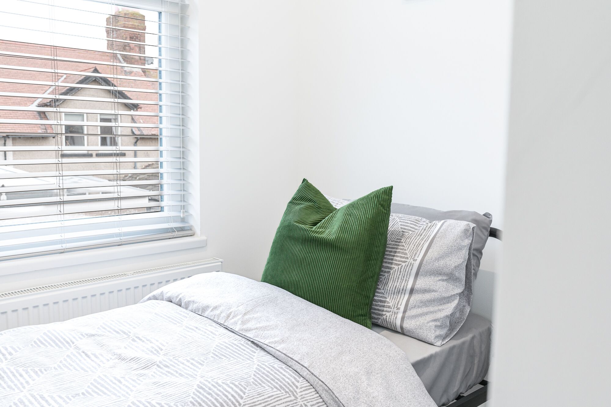 Un dormitorio con ventana, radiador y cama con almohadas.