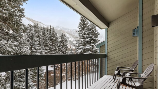 En träveranda med två Adirondack-stolar, ett metallräcke och utsikt över snötäckta träd och berg.