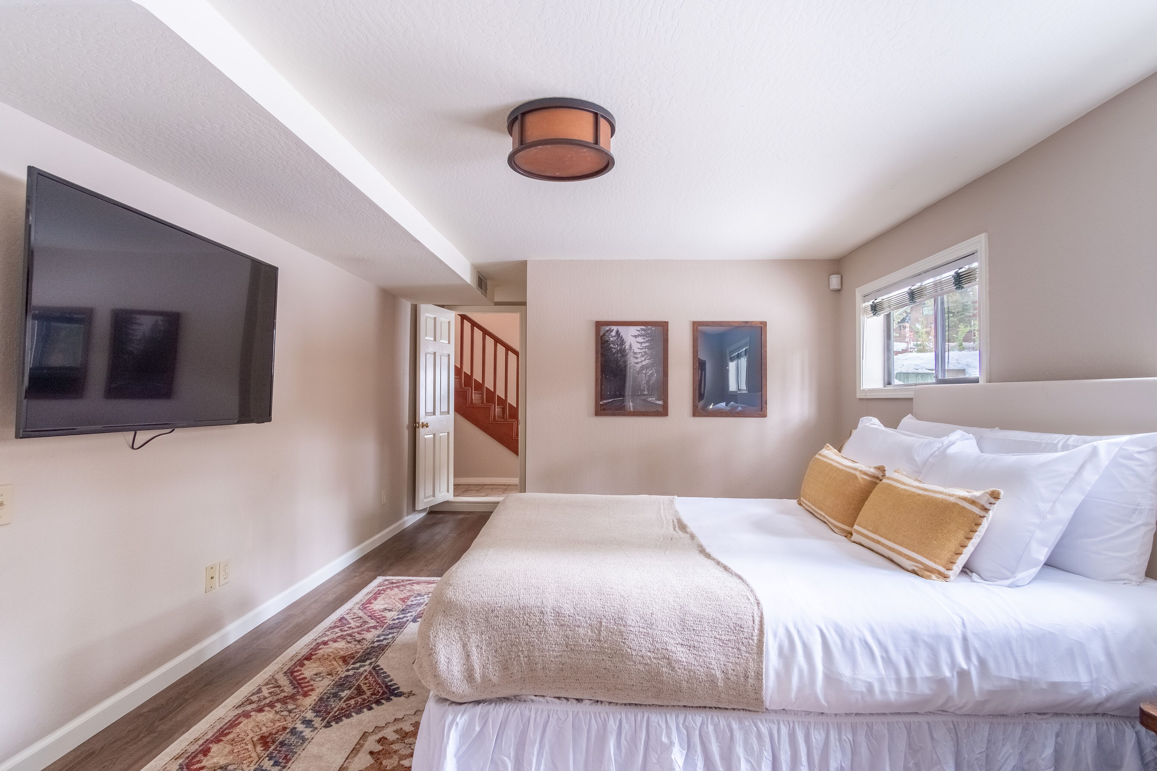 A bedroom with a large bed, a flat-screen TV mounted on the wall, and a window with blinds.