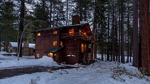 Een houten hut met een balkon en schoorsteen, omringd door sneeuw en bomen.