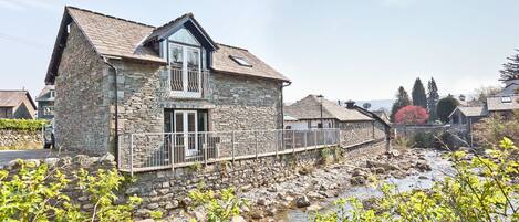 A stone house with a balcony and a view of a rocky stream.