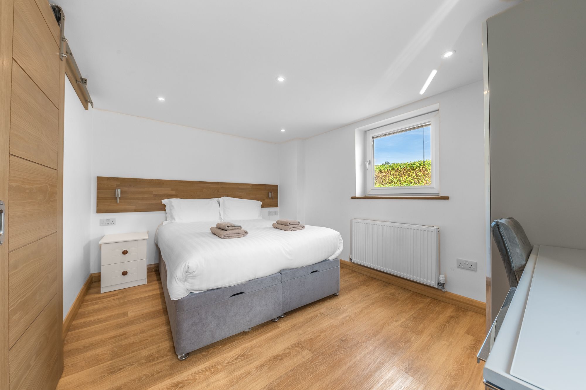 Une chambre à coucher avec un lit, des tables de chevet, un radiateur et une fenêtre donnant sur un paysage verdoyant.