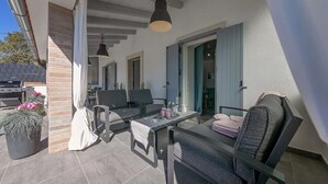 En udendørs patio med et bord, stole, en hængende lampe og en potteplante.