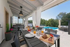 An outdoor dining area with a pool view, featuring a long table with plates, cutlery, and a variety of food items. - Villa LULU with heated pool, sauna and hot tub (Labin)