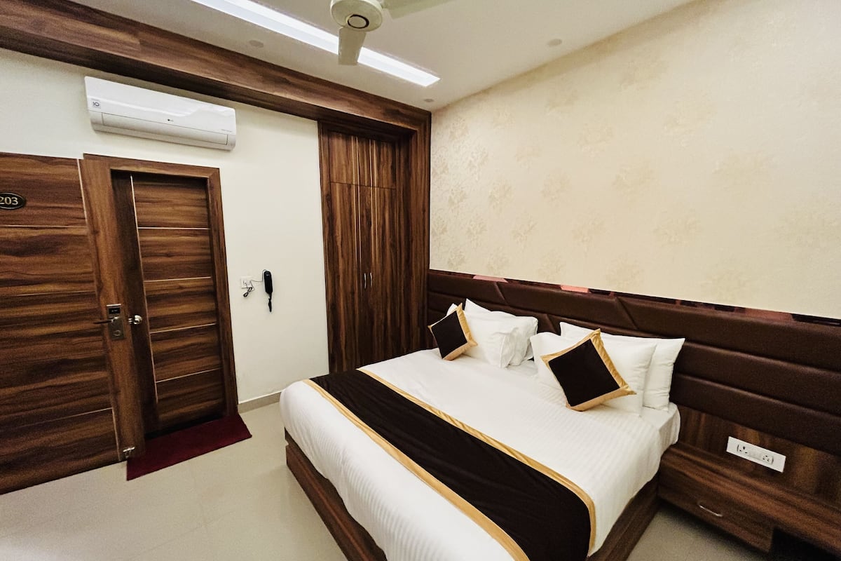A hotel room with a bed, a wardrobe, a telephone, and an air conditioning unit.