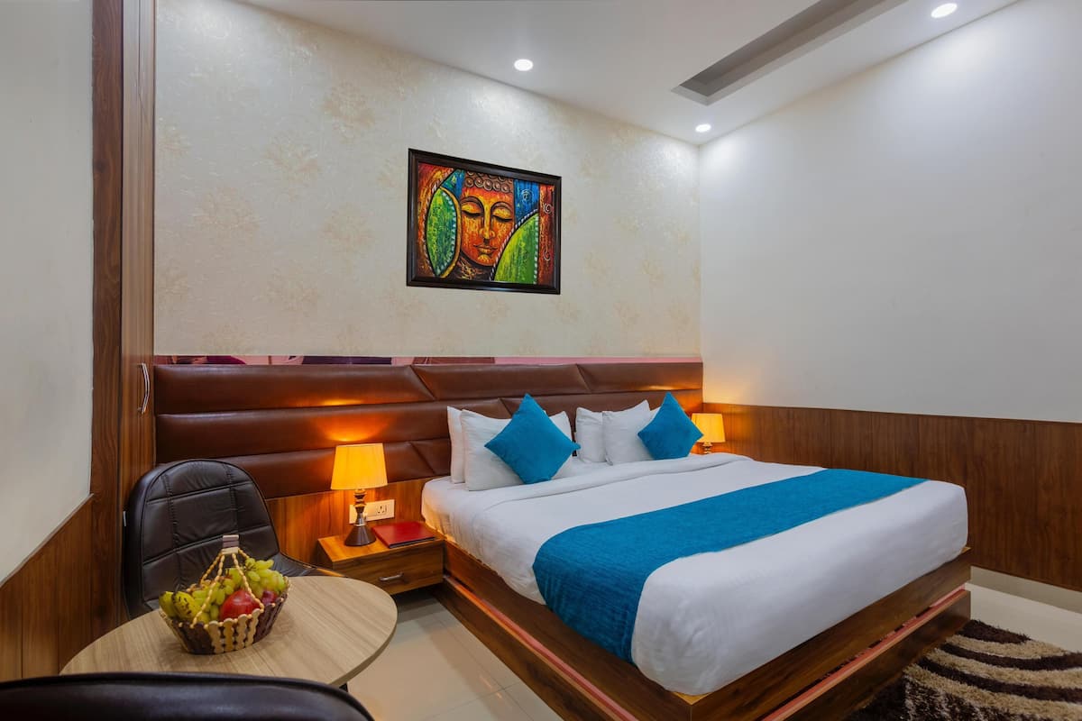 A hotel room with a large bed, a headboard, a nightstand, a lamp, a chair, and a wall art piece.