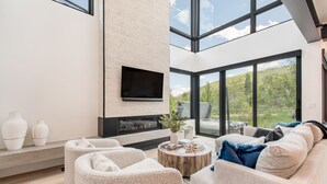 A modern living room with a fireplace, comfortable seating, and large windows offering a view of the outdoors. - Encore by AvantStay | Minutes from the Slopes in PC! w/ Hot Tub (Park City)