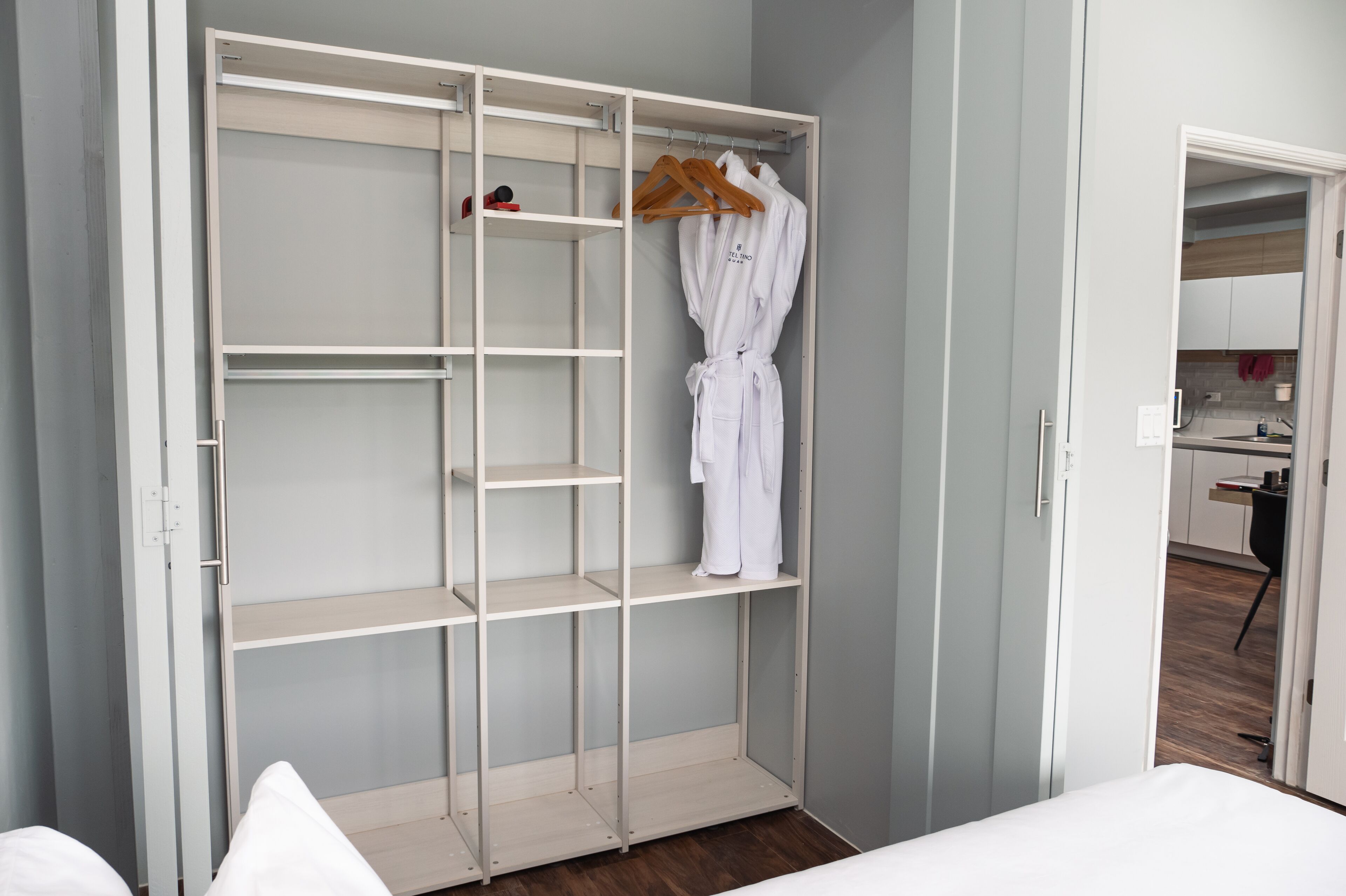 A walk-in closet with open shelves, a hanging robe, and a small kitchen area visible through an open door.