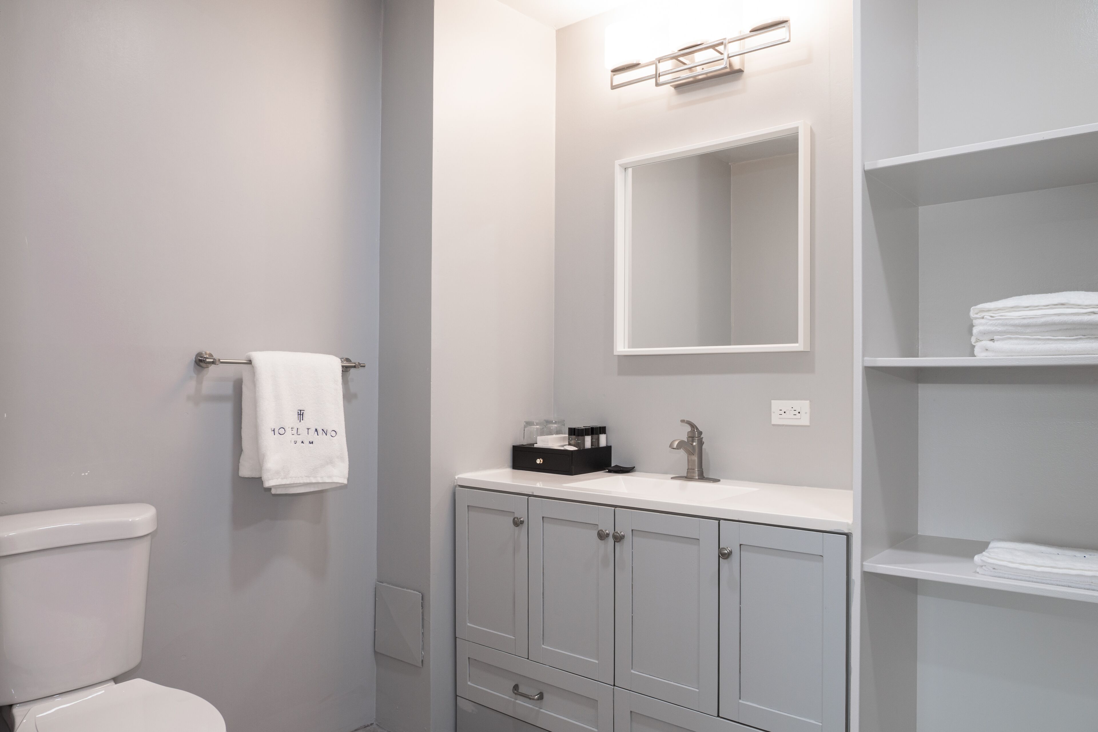 Un bany modern amb vàter, un lavabo amb mirall i un penjallatoiles amb tovallola.