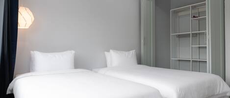 Ein Hotelzimmer mit zwei Einzelbetten, einem Kleiderschrank und einer Wandleuchte.