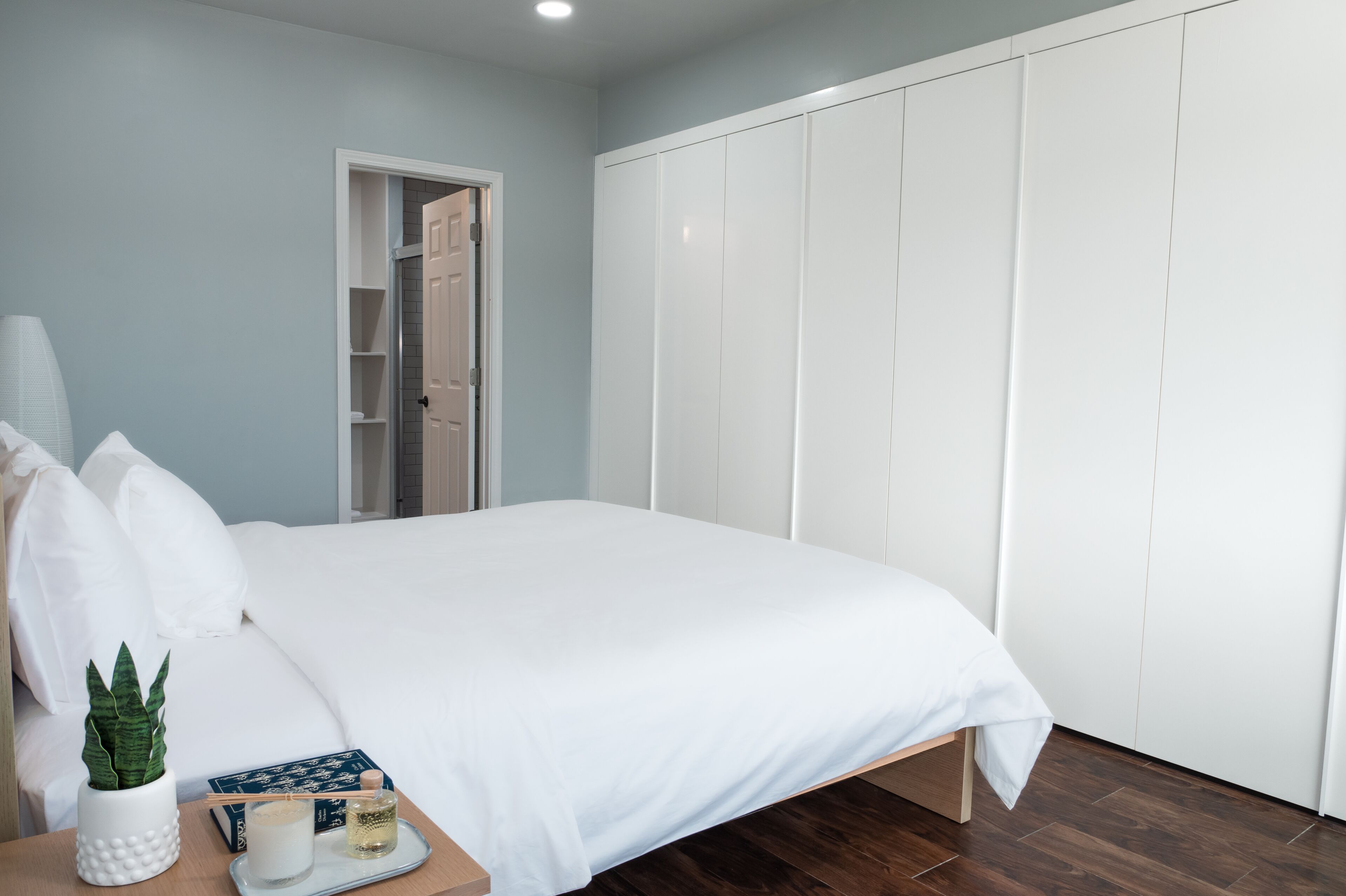 Een slaapkamer met een bed, een nachtkastje met een plant, een dienblad met kaarsen en een kledingkast.