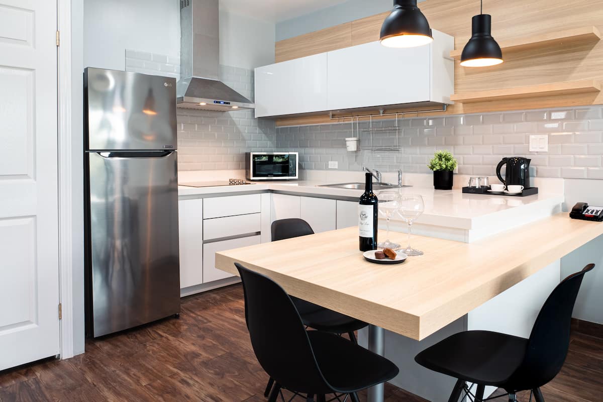 A modern kitchen with a stainless steel refrigerator, a microwave, a coffee maker, and a wooden dining table with black chairs.
