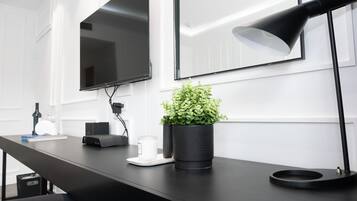 A modern workspace with a black desk, a potted plant, a lamp, and a flat-screen TV mounted on the wall.
