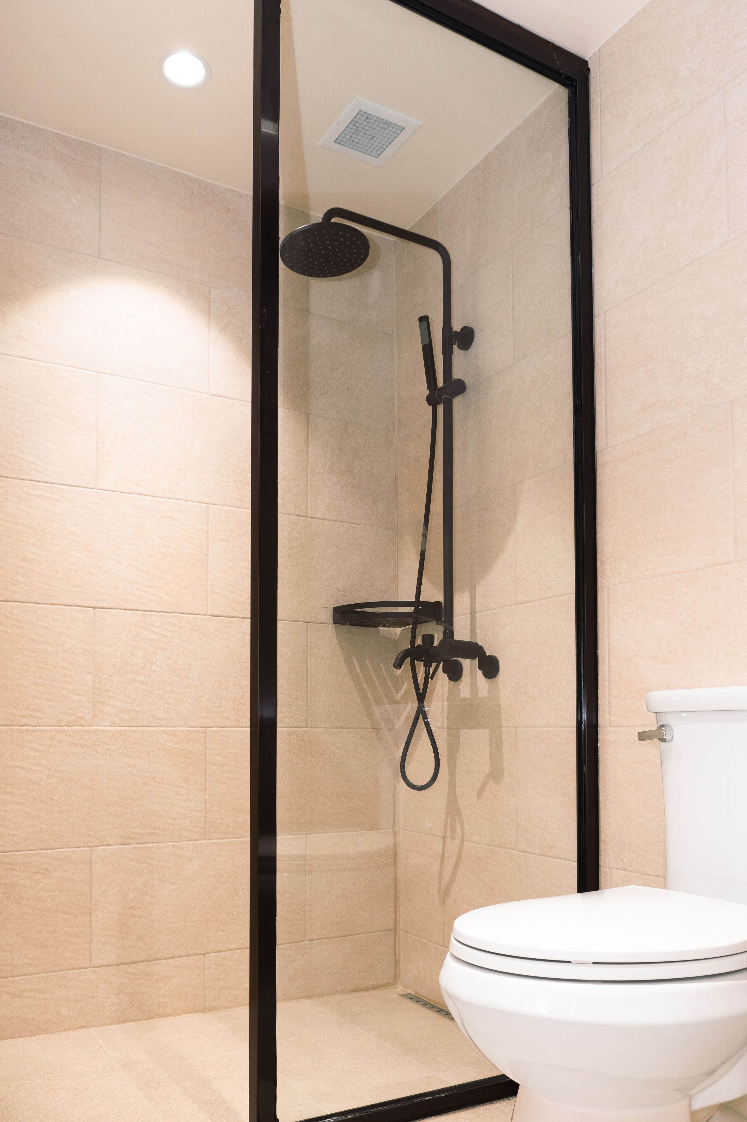 Une salle de bain moderne avec une douche à parois de verre, des toilettes blanches et des murs recouverts de carreaux beiges.