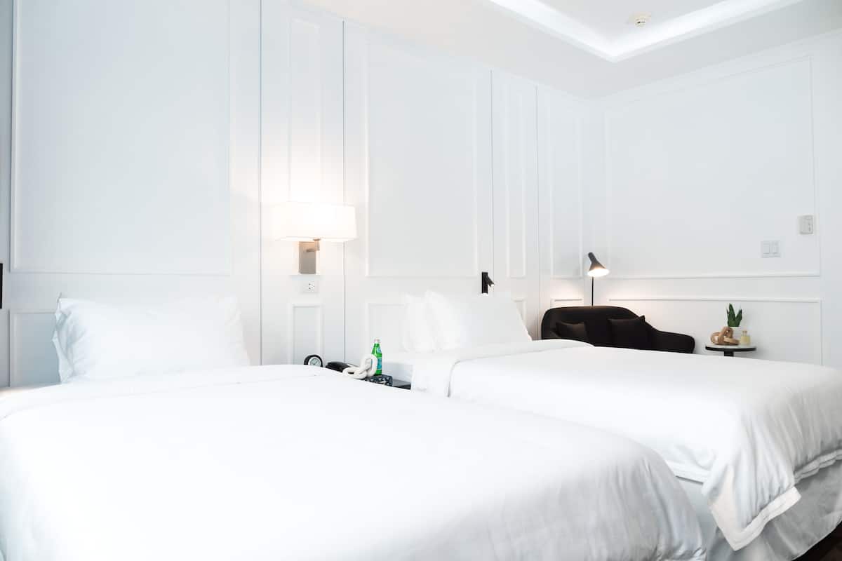 A hotel room with two beds, white walls, and a ceiling light.