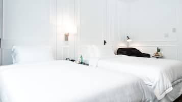 A hotel room with two beds, white walls, and a ceiling light.