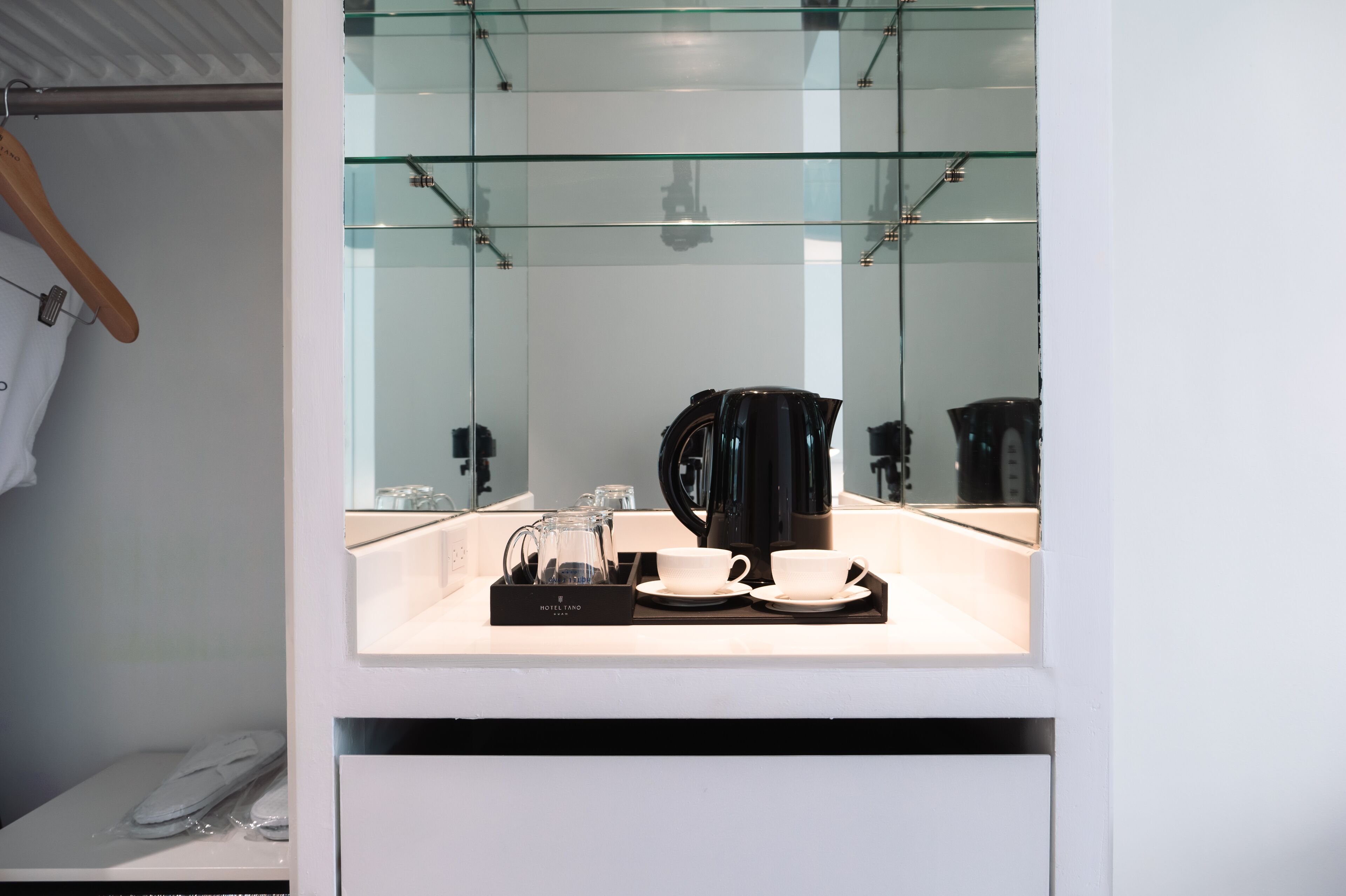 Een moderne badkamer met een douchecabine van glas, een zwarte koffiezetapparaat, twee witte kopjes en een dienblad met een glazen karaf.