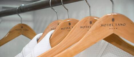 Cabides de madeira com a etiqueta "HOTEL TANO" e toalhas brancas.