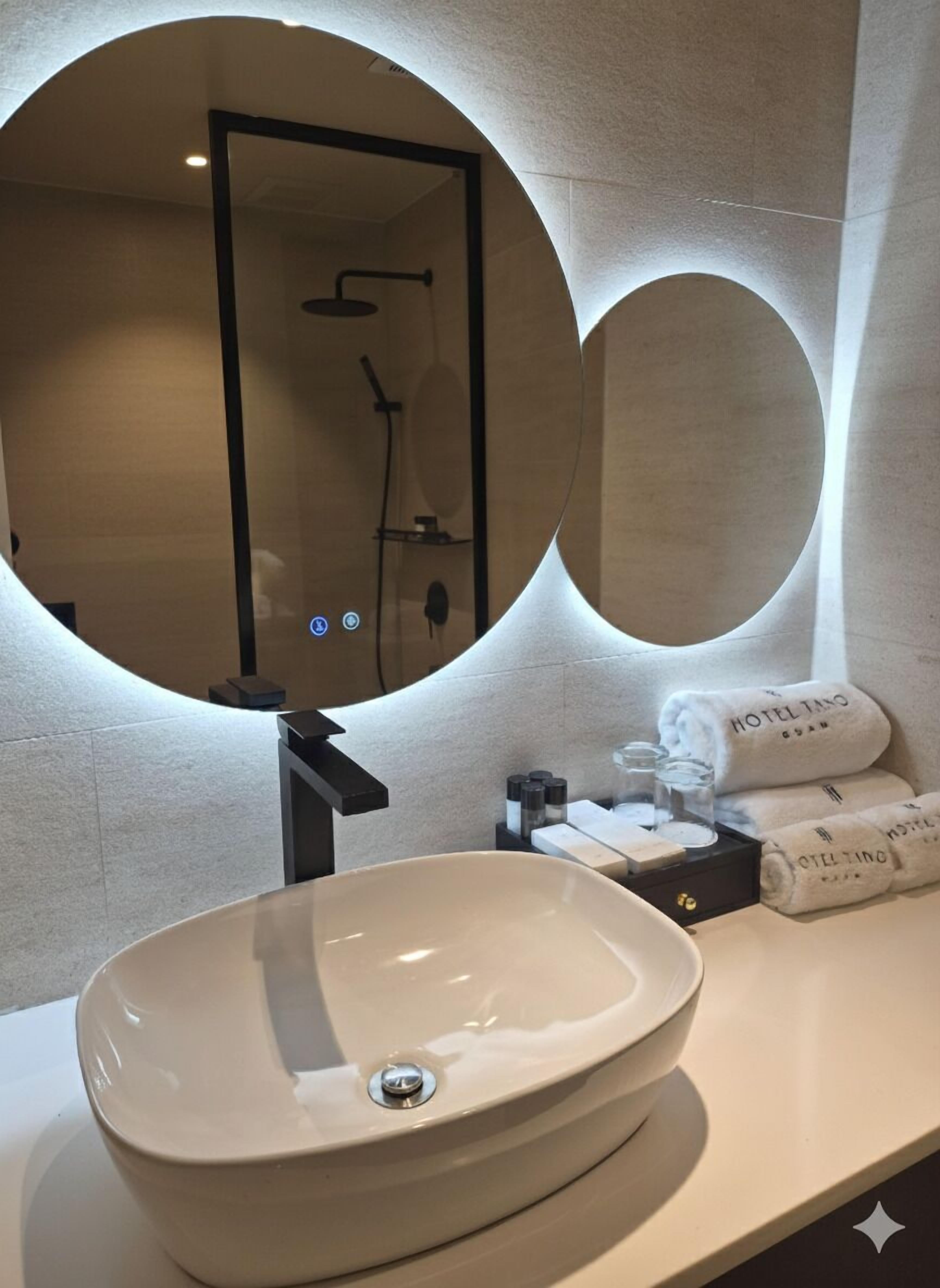A modern bathroom with a large oval sink, a round mirror, and a towel rack with neatly folded towels.