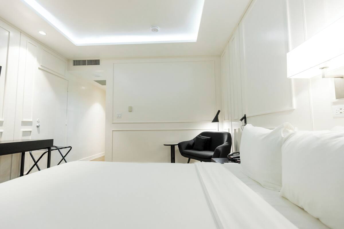A hotel room with a bed, a desk, a chair, and a small table.
