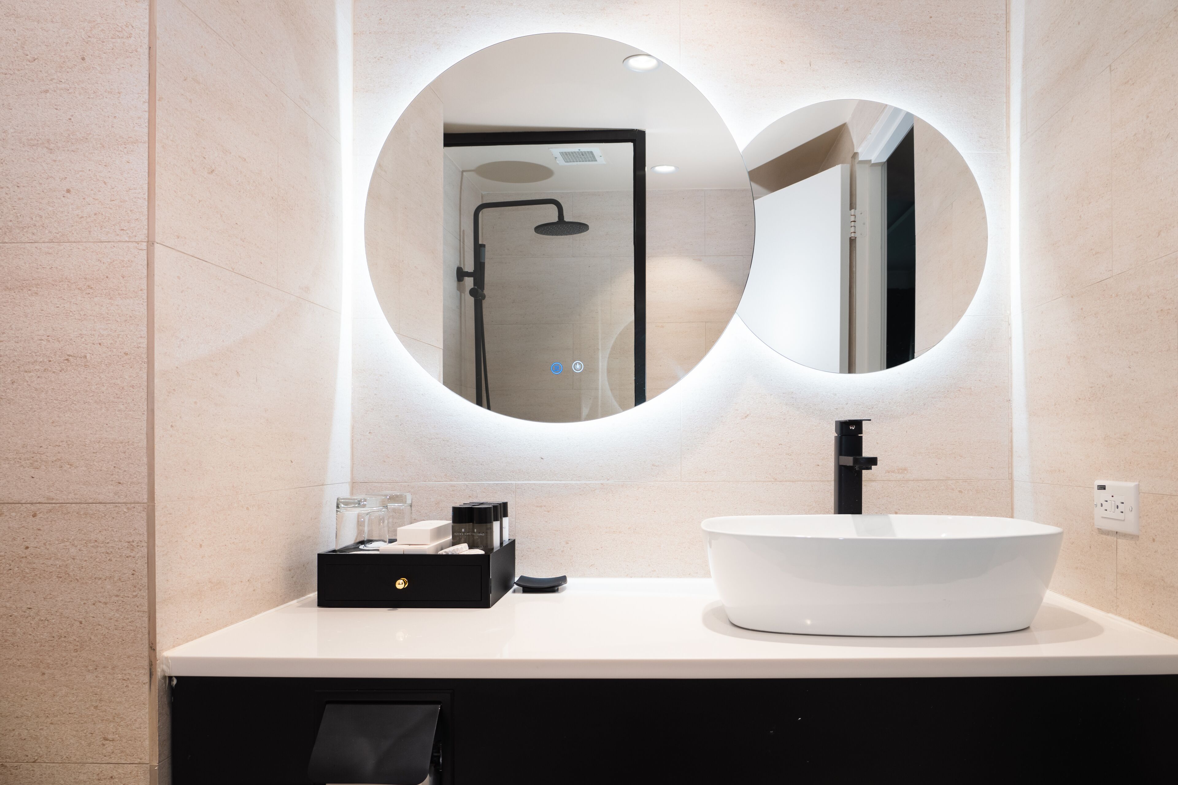 A modern bathroom with a white sink, a black faucet, and a mirror with a circular frame.
