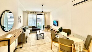 A modern living room with a sofa, coffee table, and dining area. - Rd Jade apt Neuf Avec Jardin Proche des Commodit s (La Marsa)