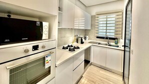 A modern kitchen with white cabinetry, a built-in oven, a microwave, and a gas stove. - Rd Jade apt Neuf Avec Jardin Proche des Commodit s (La Marsa)