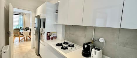 A modern kitchen with white cabinets, a gas stove, a coffee maker, and a toaster.