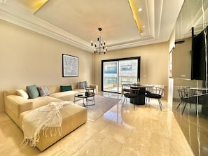 A modern living room with a beige sofa, a coffee table, and a dining area with a glass table and chairs.