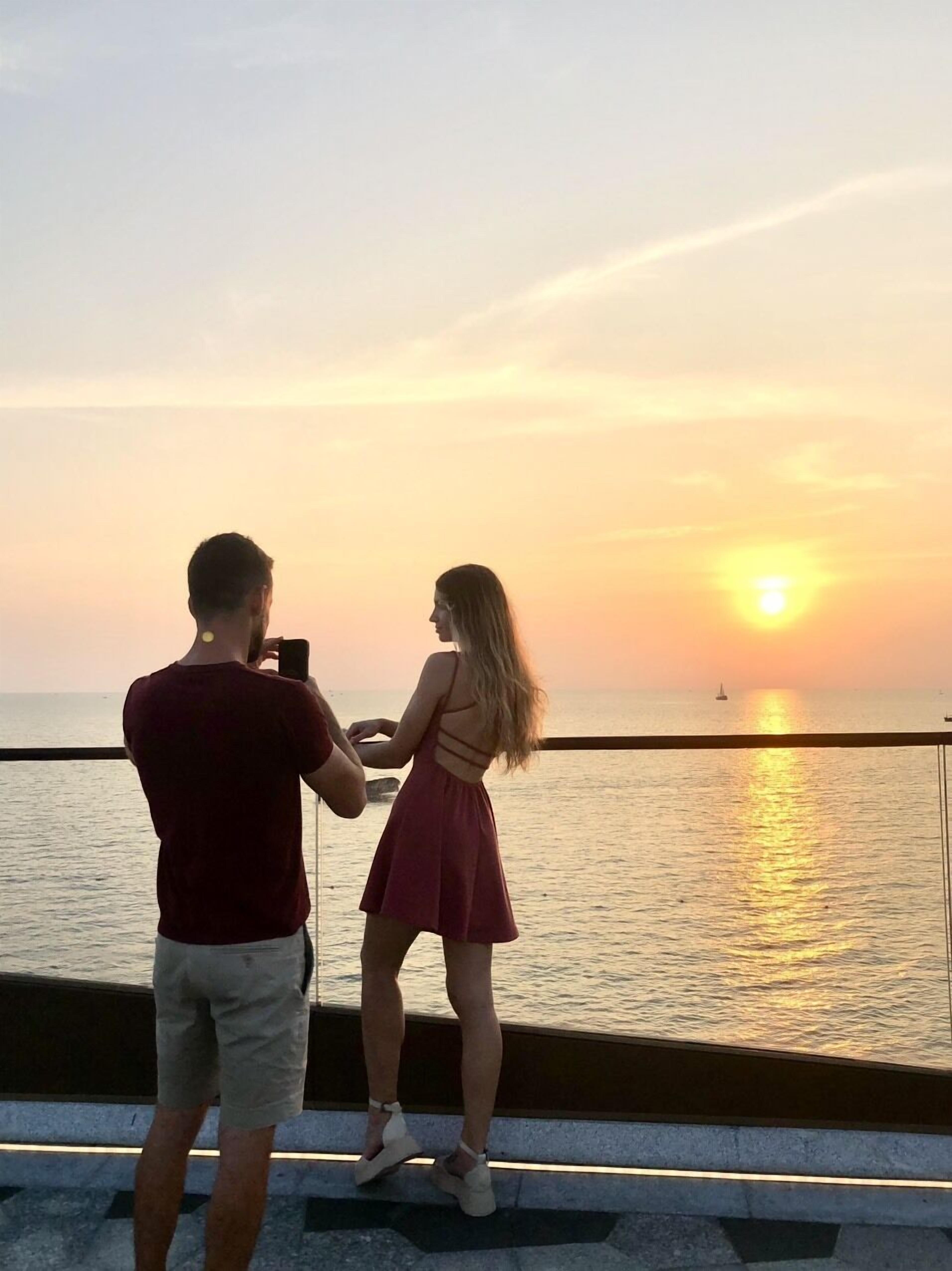 Dos personas de pie junto a la orilla al atardecer.