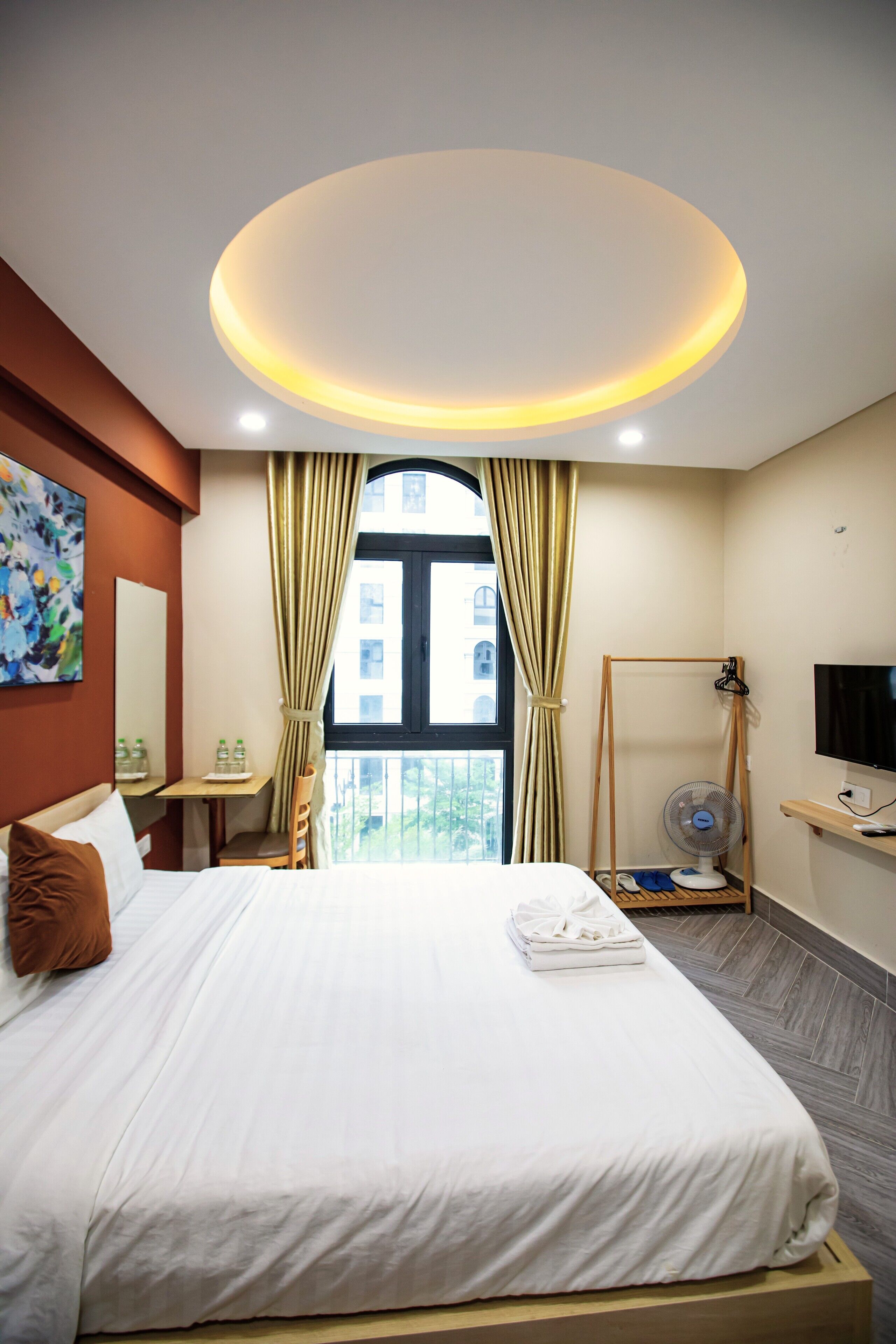 A hotel room with a bed, a TV, a fan, and a window with curtains.