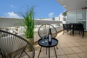 A balcony with a round table, two chairs, a bottle of wine, and a potted plant.