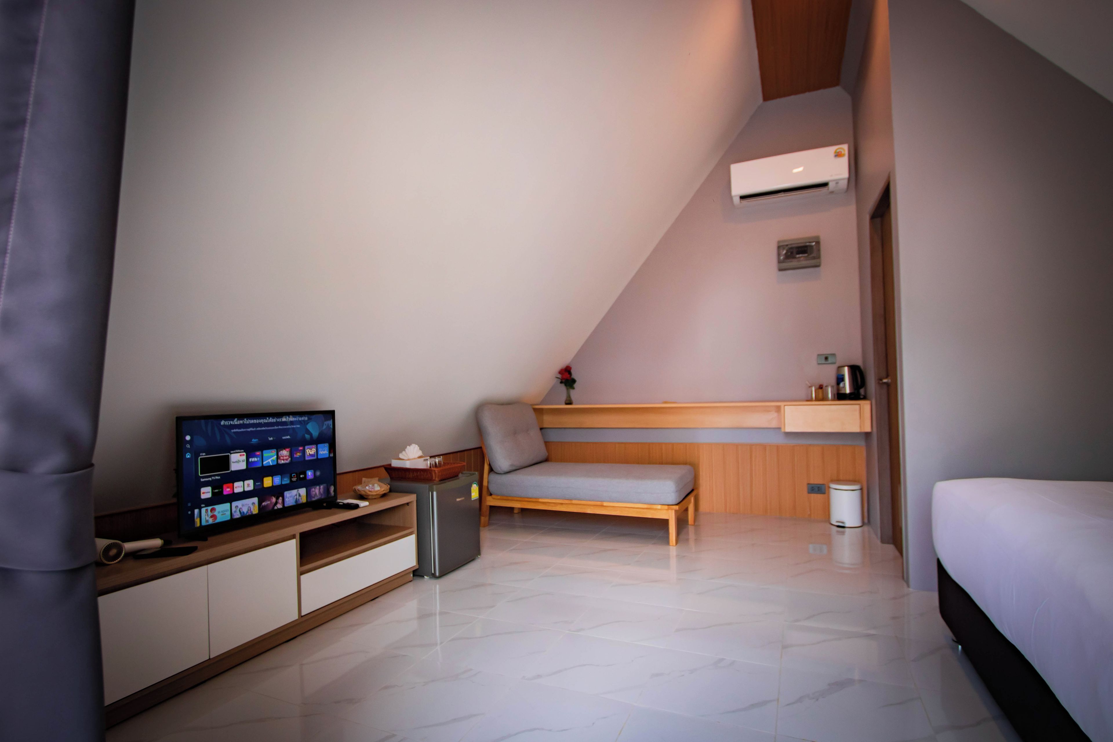 A modern bedroom with a bed, a TV, a small desk, and a bench.