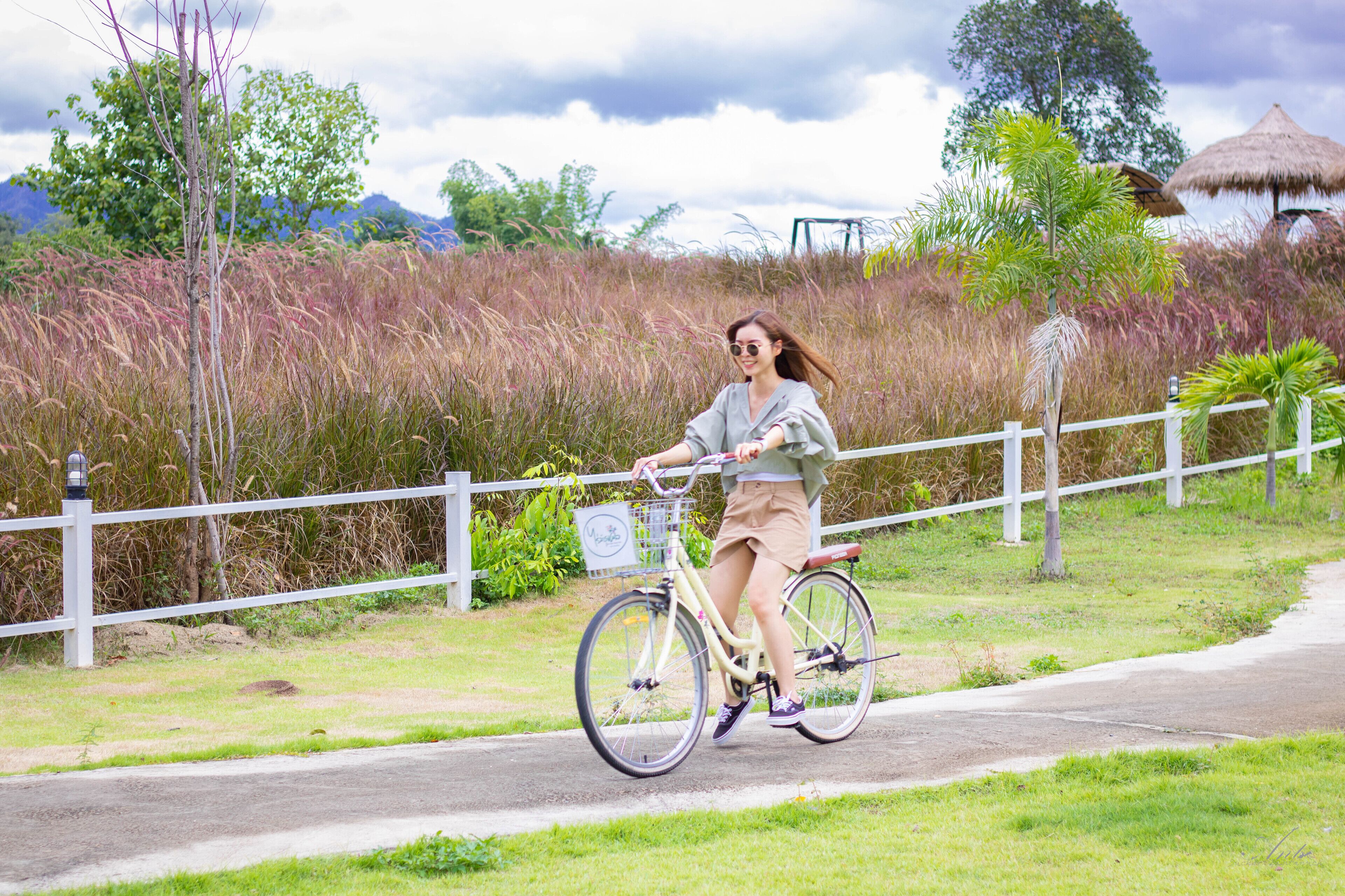 A person riding a bicycle on a paved path with a white fence and greenery in the background.