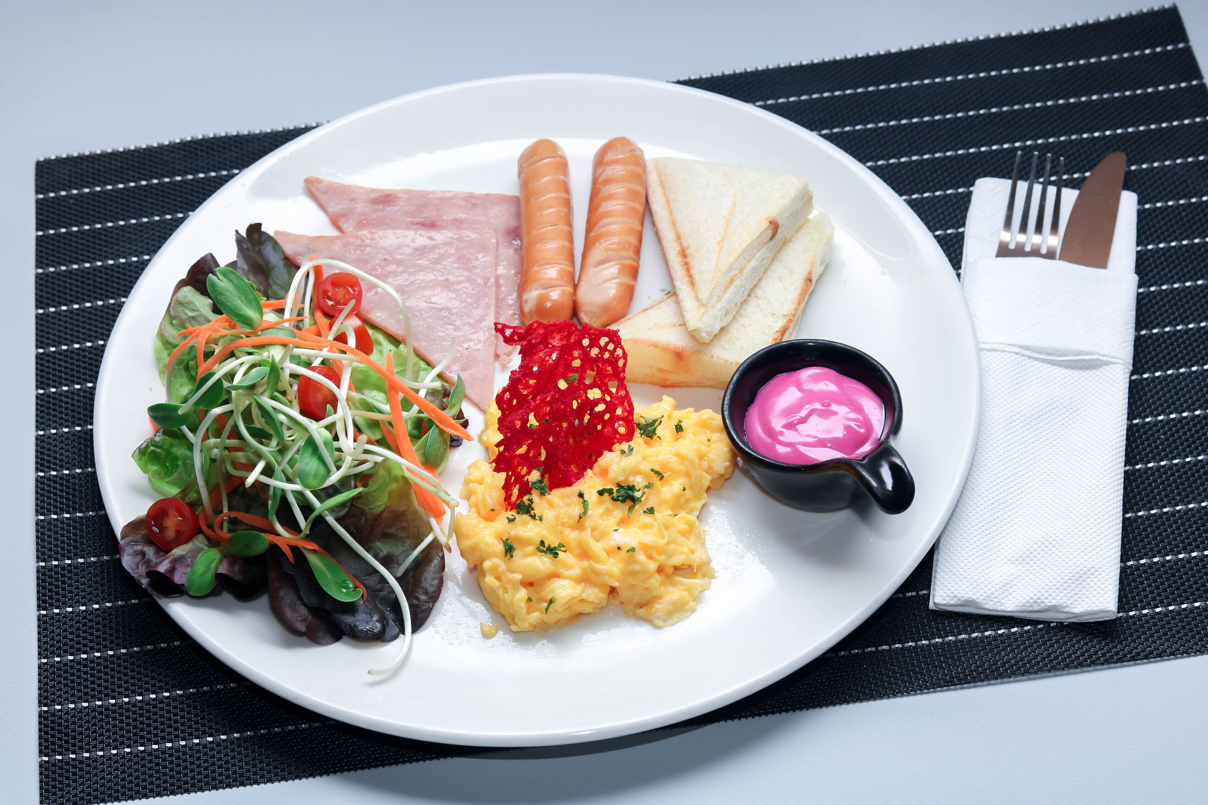 A plate with scrambled eggs, sausages, ham, and a salad.