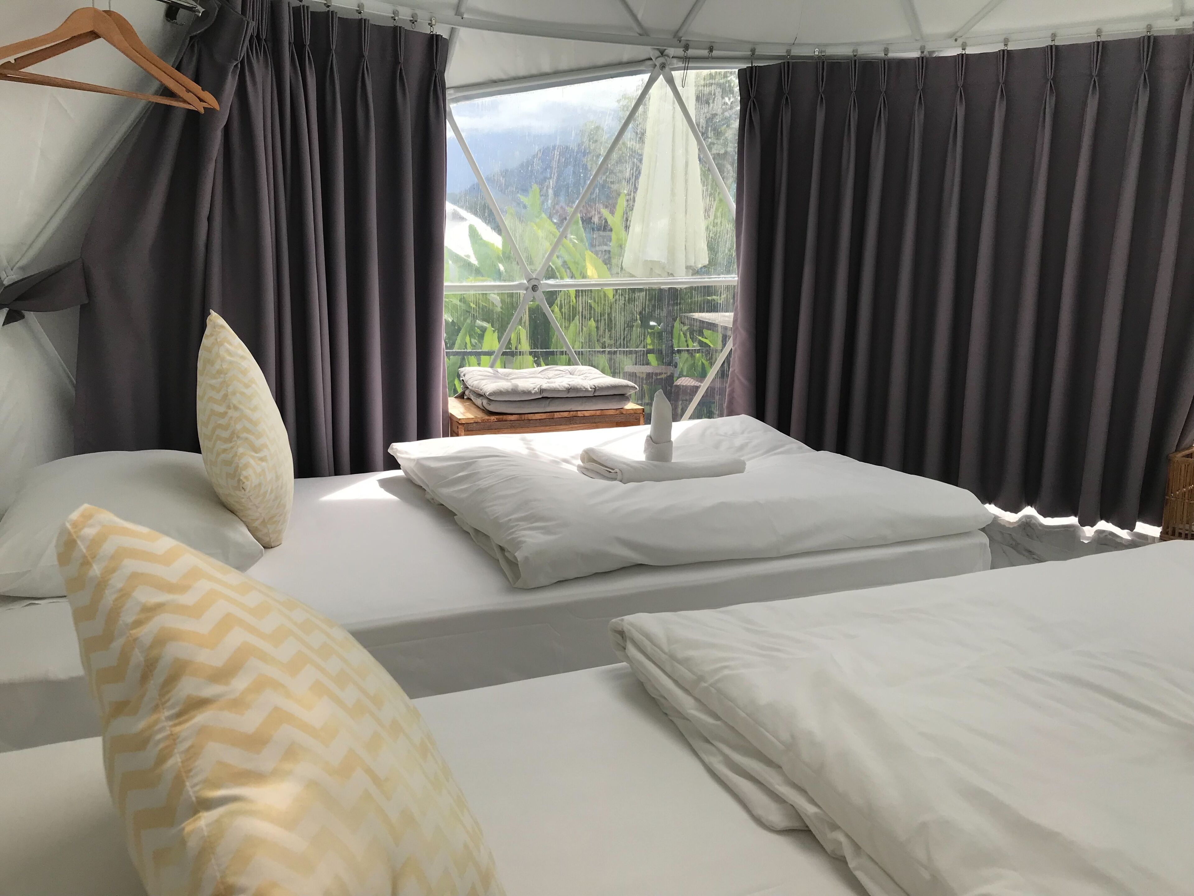 Habitación tipo tienda de campaña con cama, almohadas y vistas al follaje exterior.