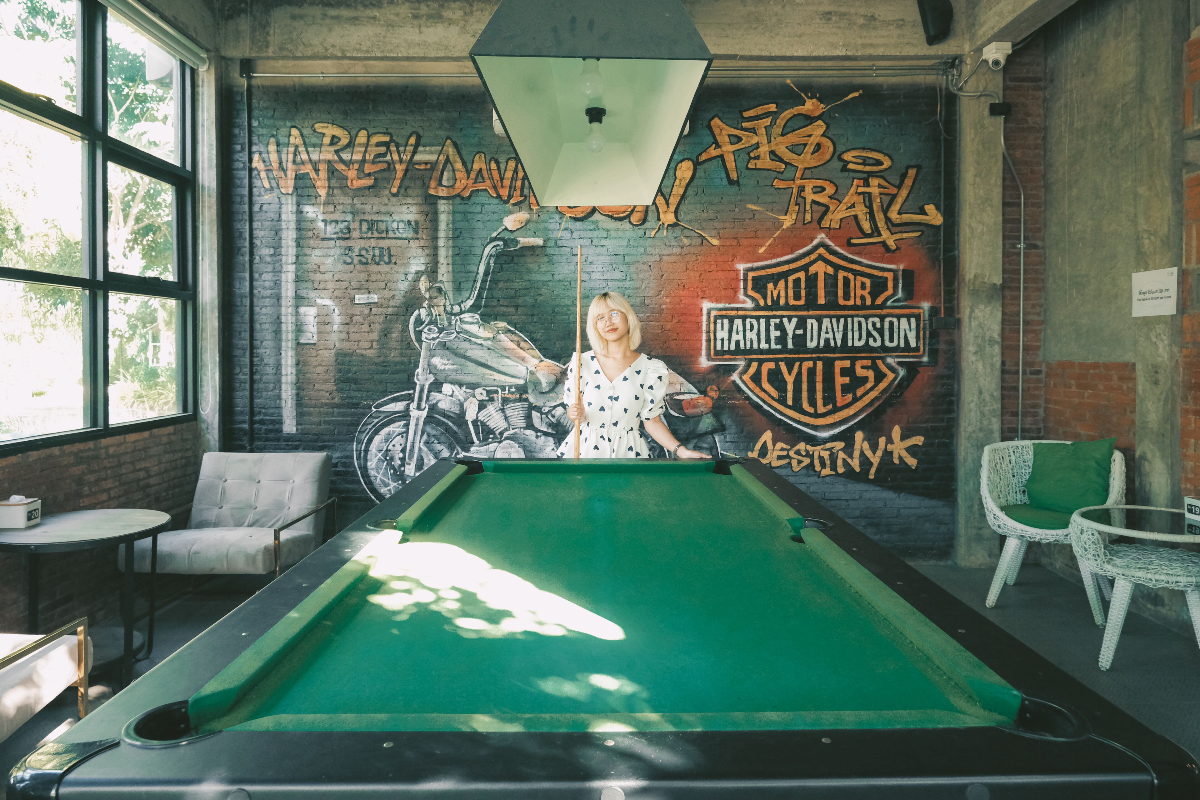 A pool table in a room with a mural of a motorcycle and text, surrounded by wicker chairs and a table.
