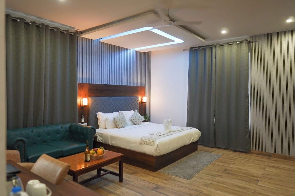 A hotel room with a bed, a green sofa, a wooden coffee table, and a small table with a fruit bowl and a bottle.
