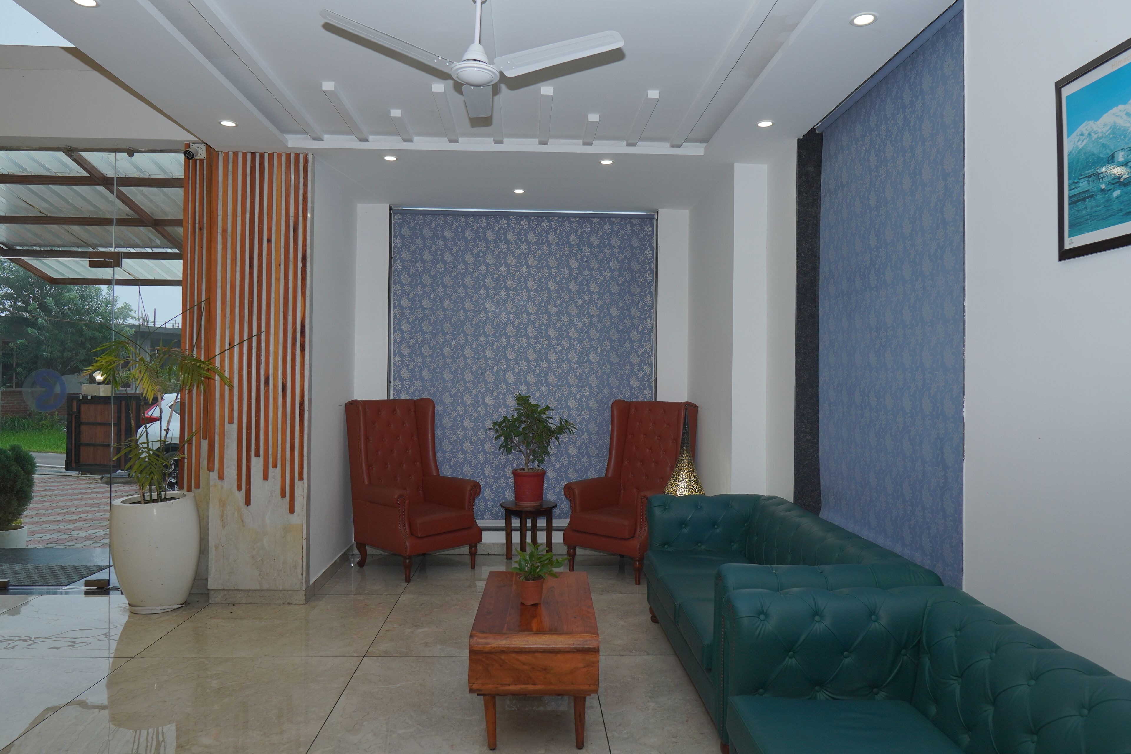 A modern living room with a ceiling fan, two red armchairs, a green sofa, and a coffee table with a plant.