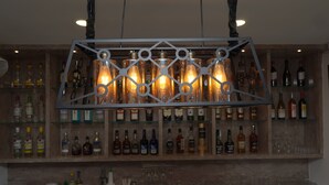 A bar area with a metal chandelier, shelves of liquor bottles, and a bar counter with glasses and a cash register. - The Abode Dharamshala (Dharamshala)