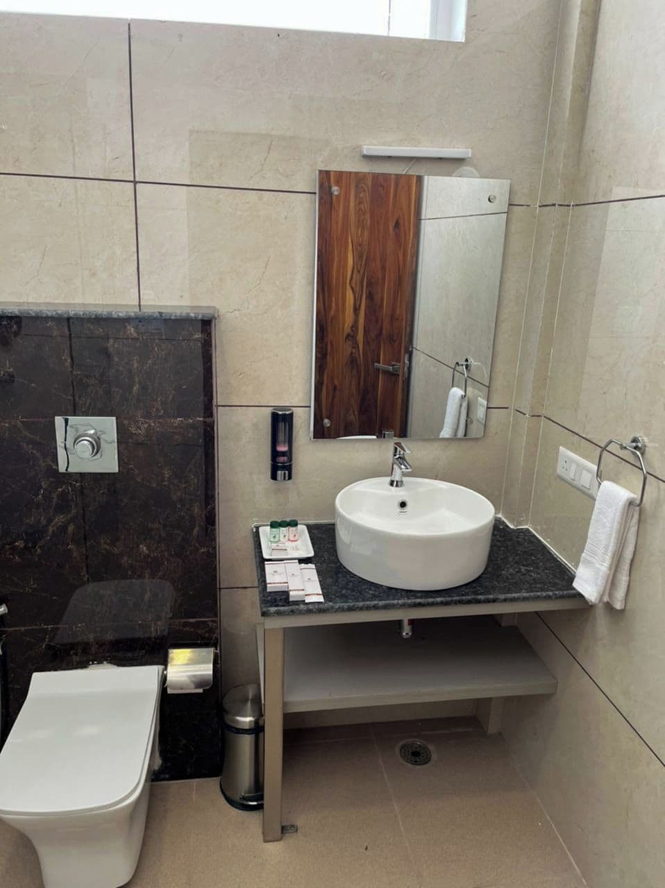 Une salle de bain avec un meuble-lavabo en marbre, un lavabo blanc, un miroir, un porte-serviettes et des toilettes.