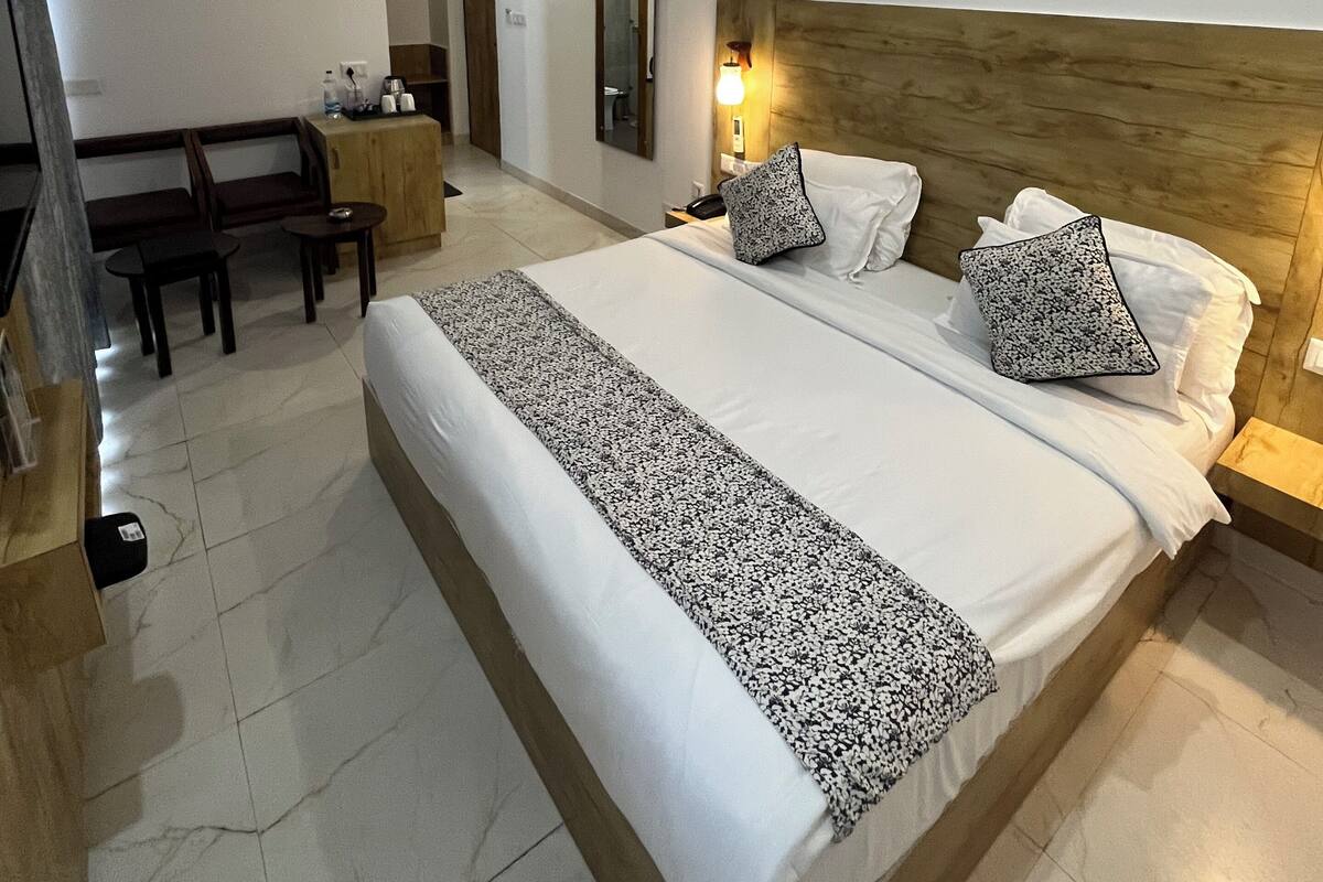 A hotel room with a large bed, bedside tables, a desk, a chair, a mirror, and an air conditioning unit.
