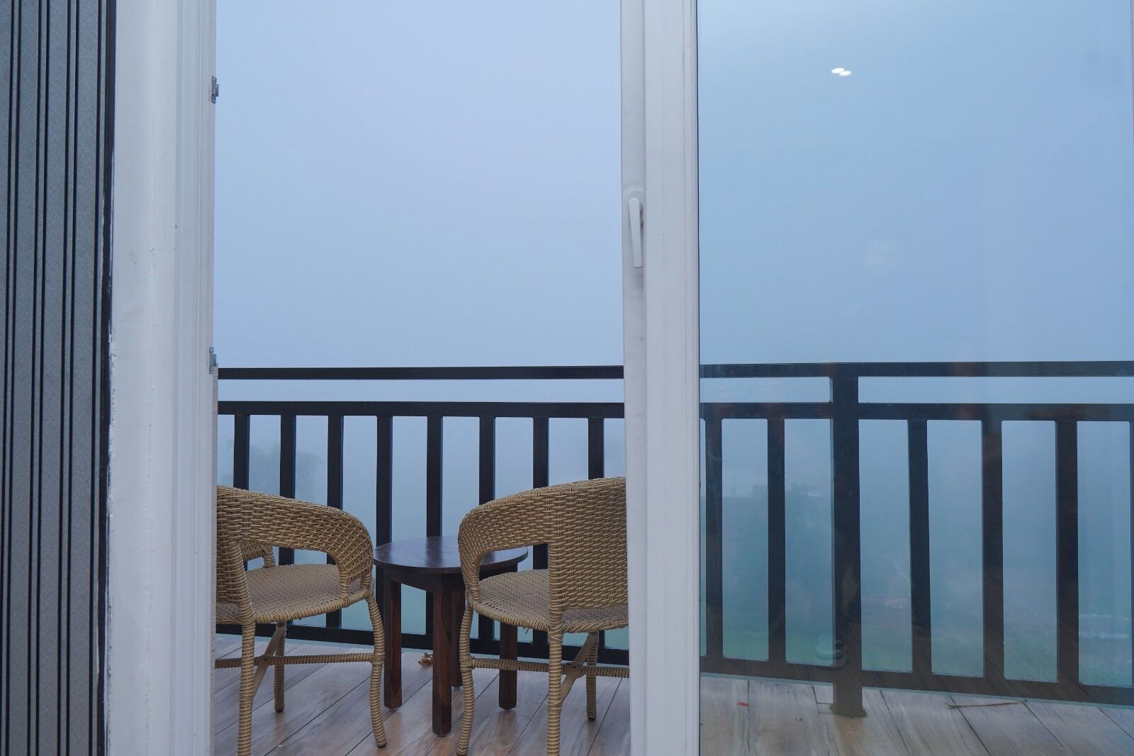 A balcony with wicker chairs and a small table, overlooking a railing and a view of the sky.